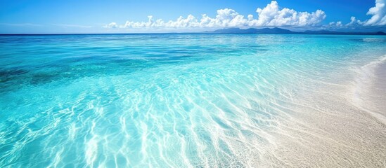 Serene tropical beach with crystal clear turquoise water and gentle waves under a bright blue sky with fluffy clouds.