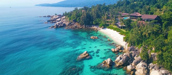 Aerial view of a picturesque rocky beach with vibrant turquoise water and lush greenery on a sunny day.