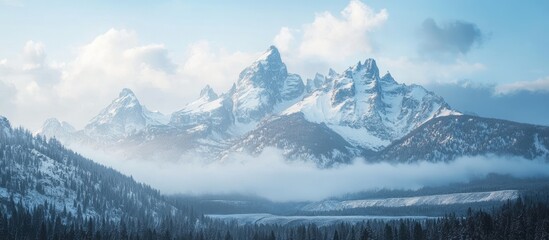Majestic mountain range shrouded in mist with snow-capped peaks against a serene sky landscape in tranquil natural setting.