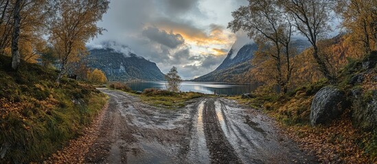 Serene autumn landscape with muddy trails leading to a tranquil lake surrounded by mountains and colorful foliage under a cloudy sky
