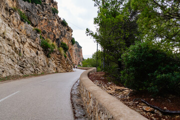 Canyamel, Mallorca, Spain (11/25/2021) - Winding coastal road with limestone cliff wall and stone barrier along Mediterranean shoreline