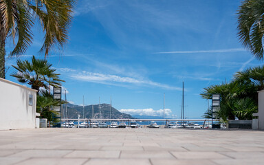 Saint-Jean-Cap-Ferrat, France - May 03, 2024: Stone Plaza with Palm Tree Gateway Framing Mediterranean Marina View