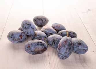 Black ripe plums with household utensils on a wooden table, close-up.