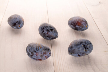 Black ripe plums with household utensils on a wooden table, close-up.