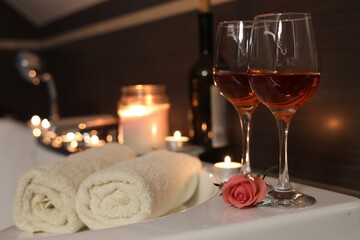 Glasses of wine, towels and rose on tub in bathroom, space for text. Romantic atmosphere