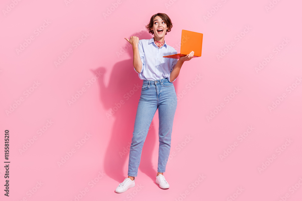Poster full length photo of astonished pretty person hold laptop look direct finger empty space isolated on