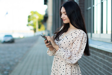 Fototapeta premium Stylish woman in polka dot dress using smartphone outdoors – modern communication, fashionable lifestyle and urban elegance in a city.