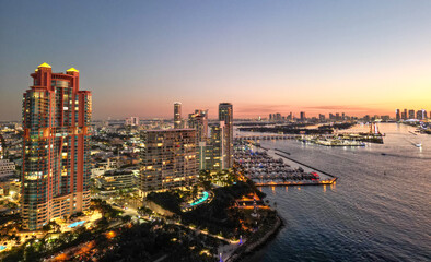 Naklejka premium Aerial panoramic view on skyscraper cityscape at night. Night city aerial. Luxury skyscraper in Miami, Florida. City skyline in evening sunset. Aerial waterfront cityscape. Miami South beach at night