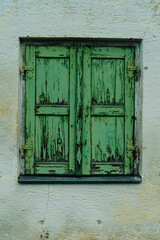 Old heavily weathered double window made of green wood on house wall.