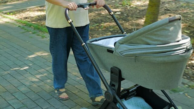 Close-up of a woman walking with a pram carrycot in the park. A mother and a child on a walk on a warm autumn day