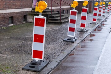 Red and white traffic barriers marking road construction zone on a rainy day