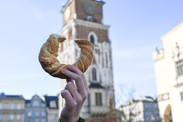 Hand holding obwarzanek krakowski prezel on Cracow Main Market Square. St. Mary's Basilica,...