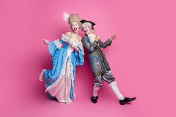 Fototapeta premium Elegant couple in vintage baroque costumes having fun against pink background, embracing classic style and fashion