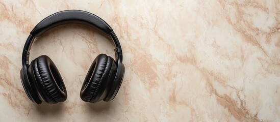 Black headphones with gel ear cushions on beige marble background with ample space for your customized text or branding