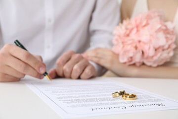 Newlyweds signing marriage contract and wedding rings on desk, selective focus