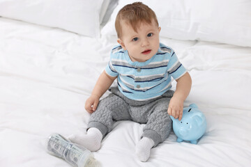 Fototapeta premium Cute little baby with money in bottle and piggybank on bed at home