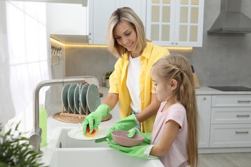 Little girl helping her mother washing dishes at home