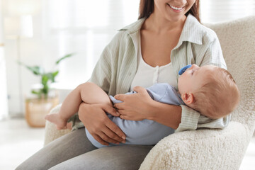 Mother with her sleeping baby in armchair at home, closeup