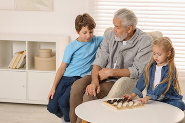 Grandpa and his grandkids playing checkers at table indoors
