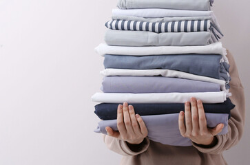 Woman holding stack of clean bed linens on light grey background