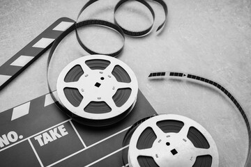 Movie clapper and film reels on grey textured table, closeup