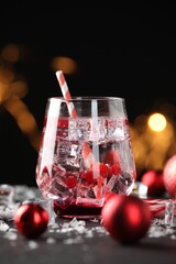 Tasty Christmas cocktail in glass, ice and decor on table against dark background with blurred lights, closeup