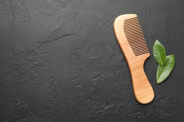 Wooden comb and leaves on dark textured table, flat lay. Space for text