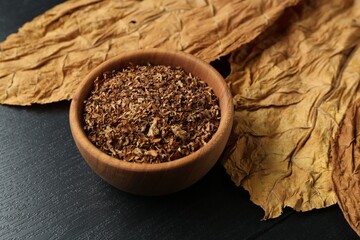 Tobacco and dried leaves on black wooden table, closeup