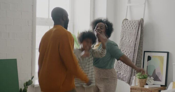 Playful African American people dad mum child dancing then falling on bed and laughing having fun at home. Family and leisure concept.
