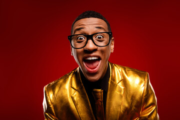 Joyful young man in gleaming gold jacket, expressing excitement against a vibrant red backdrop, perfect for holiday