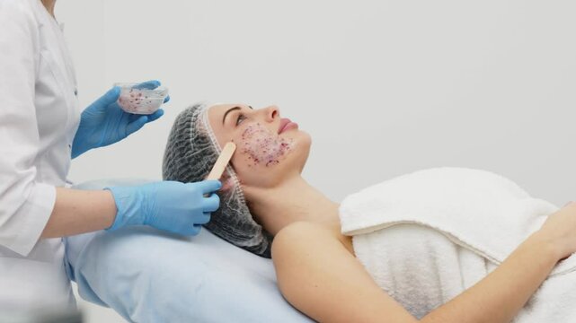 Close-up of a cosmetologist&rsquo;s hands applying an alginate mask with rose petals to a young woman&rsquo;s face in a professional beauty salon. Concept of skincare and relaxation in spa treatments.