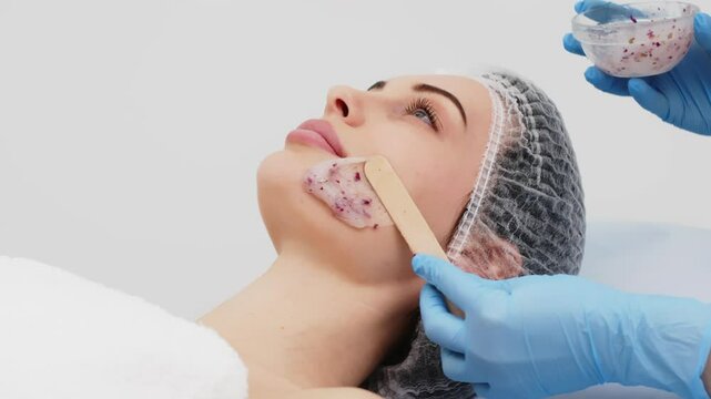 Close-up of a cosmetologist&rsquo;s hands applying an alginate mask with rose petals to a young woman&rsquo;s face in a professional beauty salon. Concept of skincare and relaxation in spa treatments.