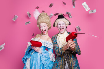 Joyful couple in vintage costumes celebrating at a theme party with flying money against a vibrant pink background