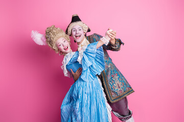 Charming couple dressed in elaborate costumes enjoying a theme party against a pink backdrop