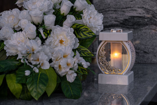 Elegant white flowers and a white candle on the grave.