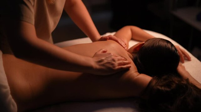 Close-up of unrecognizable massage therapist providing soothing back treatment to female client lying on massage table, delivering stress-relief wellness services in serene spa environment.