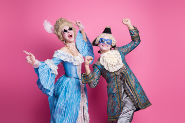 Joyful couple dressed as aristocrats pose against a vibrant pink background, capturing the fun spirit of a themed costume party