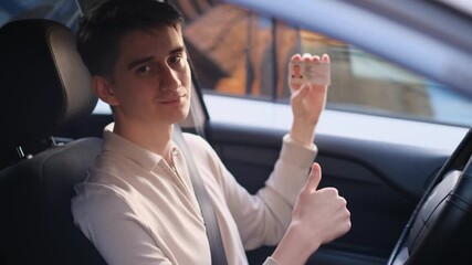 Happy novice driver showing off his driving license while sitting in a car
