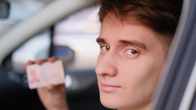 Young man shows his driving license while sitting in his car, closeup