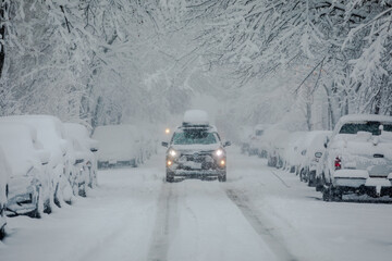 Front View of SUV Car driving through urban City during heavy Snowfall. Street, Cars and Trees...