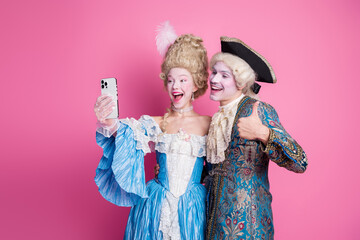 Elegant couple takes a cheerful selfie against a vibrant pink backdrop, epitomizing a fusion of...