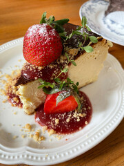Slice of cheesecake topped with rich chocolate glaze, served on a white plate and garnished with fresh strawberry