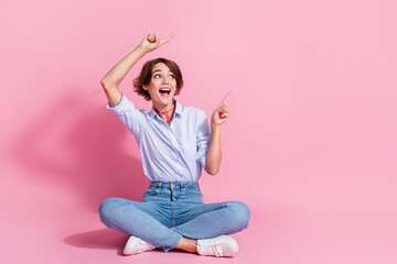 Full length photo of impressed cheerful person sit floor look direct fingers empty space isolated...