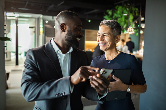 Business professionals smiling and discussing project on smartphone in modern office
