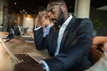 Stressed businessman working on laptop in office setting