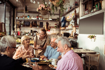 Waitress serving senior friends enjoying breakfast in a cozy cafe