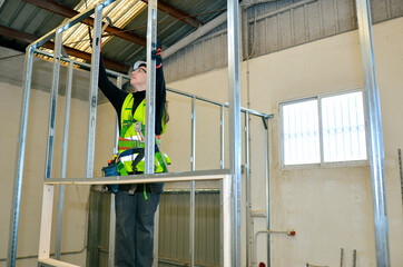 Construction worker mounting plasterboard on metal frame