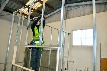 Construction worker mounting plasterboard on metal frame