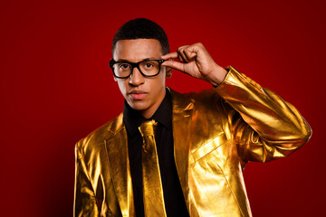 Young man in a golden suit with glasses posing against a red background, exuding charisma and style.