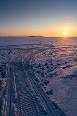 An ice field stretching into the distance with traces of snowmobiles and human footprints.